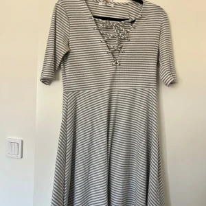Randig kortklänning med snörning - Superfin kortklänning från Glamorous i grått och vitt med smala ränder. Klänningen har snörning vid v-ringningen och halvlånga ärmar.