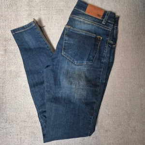 Blå skinny jeans med dragkedja - Säljer ett par blå skinny jeans från Lager 157, modell Skinny Zip. Jeansen har dragkedja vid benslut, klassisk femficksdesign och är tillverkade i stretchig denim av bomull och elastan. Perfekta för dig som gillar en tight passform och stilren look.