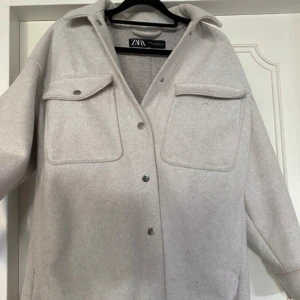 Vit kappa från Zara i ullmix  - Kappa från Zara i beige ullmix med stora bröstfickor och tryckknappar framtill. Rak passform och klassisk krage, perfekt för lager-på-lager. Snygg och enkel att styla till olika outfits. Inte så mycket använd, max 3 gånger. Saknar två knappar, en vid en ficka och den andra längst ner(se bilder). Annars inget mer synligt. Är i storlek xs men sitter som S. Pris kan diskuteras, skriv om mer frågor💗