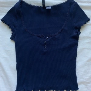 Marinblå ribbad topp - Supersöt marinblå ribbad topp från H&M Divided. Toppen har tre knappar framtill som går att öppna och stänga hur man vill!!