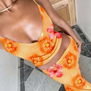 Orange blommigt sett  - Snygg långkjol och topp i orange med stora blommor i rött och gult. Klänningen har smala axelband, djup urringning och figurnära passform. 