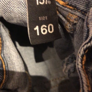 Blå jeans med hög midja, storlek 160 - Säljer ett par blå jeans från H&M i storlek 160. Byxorna är lågmidjade med dubbla knappar, raka ben och stora fickor fram. Klassisk denim med ljus tvätt och bekväm passform, perfekta till vardagslooken.