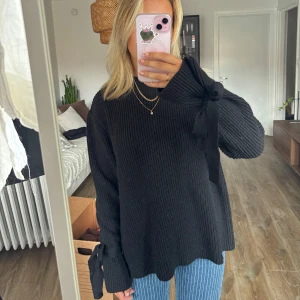 Svart stickad tröja med rosetter - Svart stickad tröja med rosetter vid ärmsluten. Storlek L men känns mer som en mindre storlek med loose fit 