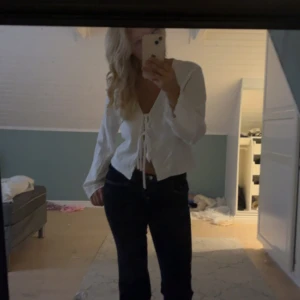 Vit omlottblus med snörning - Säljer en vit omlottblus med snygg snörning framtill och v-ringning. Blusen har långa, lätt utsvängda ärmar och är croppad i modellen. Perfekt för dig som gillar en stilren och trendig look.