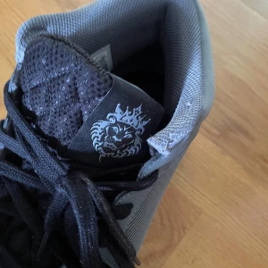 Nike grå sneakers med svart mesh - Nike sneakers i grått och svart med coolt lejonmotiv på plösen. Ovandelen är i mesh och syntet, med svarta snören och vit sula med synlig Air-enhet. Snygg sportig look och riktigt bekväma för vardagen. Pris kan diskuteras