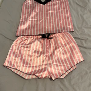Rosa och vita randiga pyjamasshorts - Snygga pyjamasshorts i glansigt material med rosa och vita ränder. De har elastisk midja och en svart rosett framtill. Perfekta för mysiga kvällar hemma och har en loose fit för extra komfort.