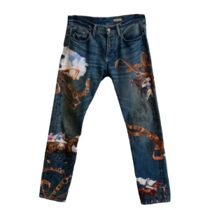 Unika blå jeans med cowboy-motiv - Säljer ett par blå jeans med coolt tryck av cowboys, moln och läderdetaljer. Jeansen har klassisk femficksmodell och raka ben. Perfekta för dig som vill sticka ut med en kreativ och konstnärlig look.