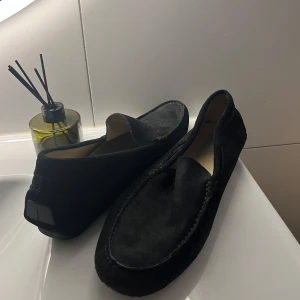 Svarta mockaloafers med rund tå - Stilrena svarta loafers i mocka med klassisk rund tå och diskreta sömmar. Skorna har platt sula och en enkel slip-on design som gör dem lätta att ta på. Perfekta för en clean och avslappnad look. Skorna kommer ifrån Frankrike! Pris går att diskutera!