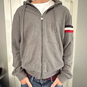 Grå Moncler hoodie med dragkedja - Snygg grå hoodie från Moncler med hel dragkedja, huva och kängurufickor. Köpt hos Merch Sweden! 