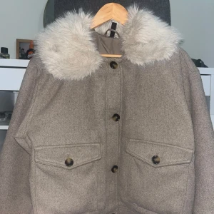 Kappa - Snygg beige jacka i ullmix med stora knappar och två rejäla fickor framtill. Kragen är klädd i mjuk, ljus fuskpäls som ger en extra cozy vibe. Perfekt för kyliga dagar när du vill vara både varm och stilren.