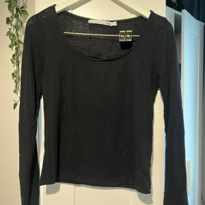 Svart ribbad långärmad topp med spets - Svart långärmad topp från 157 med ribbad struktur och rund halsringning. Snygg detalj med svart spetskant vid halsen som ger en extra touch. Tunn och stretchig, perfekt att styla med jeans eller kjol. Inte använd alls.