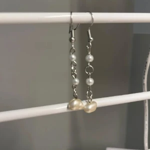 Långa örhängen med pärlor - Säljer ett par snygga långa örhängen med silverfärgade detaljer och små vita pärlor på rad. Nederst sitter en större oregelbunden pärla som ger ett unikt och trendigt uttryck. Perfekta för dig som gillar stilrena men ändå iögonfallande smycken. Handgjort 