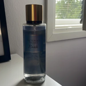 Victoria's Secret Rush Body Mist - Fräsch body mist från Victoria's Secret i doften Rush. Flaskan är genomskinlig med blå etikett och guldfärgat lock. Rymmer 250 ml och är perfekt för dig som gillar fruktiga och träiga toner.