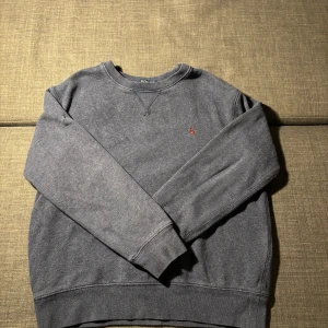 Grå sweatshirt från Polo Ralph Lauren - Mysig grå sweatshirt från Polo Ralph Lauren med klassisk rund hals och broderad röd logga på bröstet. Tröjan är helt fläckfri och i mycket bra skick, storlek 152