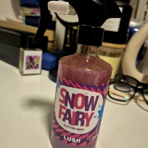 Lush Snow Fairy Glitter Mist 250ml - Snow Fairy Glitter Mist från Lush är en rosa, glittrig kroppsspray i en plastflaska med spraymunstycke. Doften är söt och lekfull, och flaskan rymmer 250 ml. Perfekt för dig som vill ha extra shimmer och en magisk känsla i vardagen. Oanvänd.