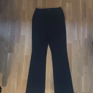 Svarta bootcut kostymbyxor BikBok - Svarta kostymbyxor från BikBok i storlek 38. Byxorna har bootcut-modell med vida ben och klassiska hällor för bälte. Snygg och stilren look som passar perfekt till en trendig outfit. Materialet är mjukt och följsamt för en bekväm känsla.