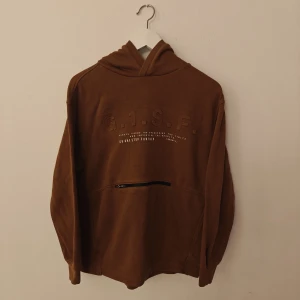 Zara hoodie - Säljer en brun hoodie från Zara med broderad text G.I.S.F. framtill och en praktisk dragkedjeficka. Tröjan har huva, långa ärmar och är tillverkad i mjuk bomullsblandning. Perfekt för chill dagar och snygg till jeans eller joggers.