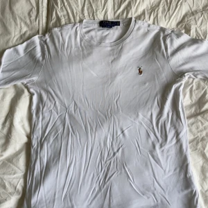 Vit t-shirt Polo Ralph Lauren slim fit - Snygg och klassisk vit långärmad tröja från Polo Ralph Lauren. Säljs helt ny för runt 1300kr. Tröjan är i storlek 170 och har det ikoniska broderade Polo-emblemet på vänster bröst. Tillverkad i mjuk och bekväm bomull med bra passform.  💡 Tröjan är använd men i gott skick – inga hål eller fläckar. Den är något skrynklig på bilden men kan enkelt slätas ut med strykning eller ånga.  ✅ Äkta vara ✅ Perfekt till vardag eller under skjorta ✅ Skick: Begagnad, mycket bra 
