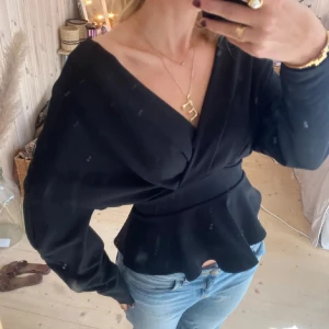 Svart omlottblus med knyt i midjan - Supersnygg svart omlottblus med långa puffiga ärmar och volang nertill. 