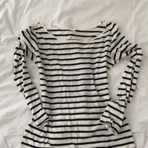 Randig långärmad tröja i bomull - Snygg långärmad tröja med svartvita ränder och rund hals. Tröjan är i mjuk bomull och har en klassisk, avslappnad passform. Perfekt att styla med jeans eller kjol för en enkel och stilren look.