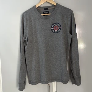 Grå långärmad tröja Abercrombie S - Snygg grå långärmad tröja från Abercrombie & Fitch med tryckt logga och siffran 92 på bröstet. På ena ärmen står det 'Abercrombie' i rött och vitt. Tröjan har rund hals och är i mjuk bomull, perfekt för chill dagar.