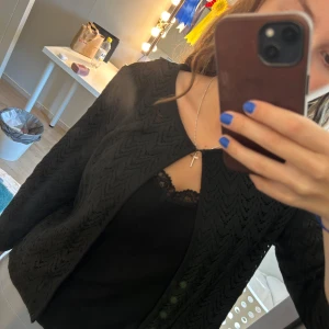 Svart stickad cardigan jacka - Säljer en svart trekvarts ärmad cardigan jacka med snyggt hålmönster och diskret knäppning. Det står tyvärr inte märke eller storlek men skulle gissa på s/m