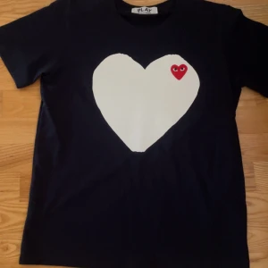 Svart Comme des Garçons Play t-shirt - Svart t-shirt från Comme des Garçons Play med stort vitt hjärta och rött hjärta med ögon på bröstet. Klassisk rund hals och korta ärmar. Perfekt statement-plagg för dig som gillar streetstyle och coola prints.