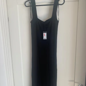 Svart ribbad långklänning XS - En svart långklänning med ribbad struktur och breda axelband. Klänningen har en enkel och stilren design som passar perfekt för dig som gillar minimalistiskt mode. Materialet känns mjukt och följsamt mot kroppen.