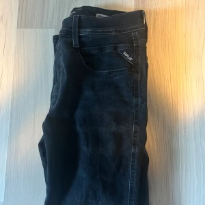 Replay Anbass Hyperflex svarta jeans - Svarta Replay Anbass Hyperflex jeans med slim fit. Klassisk femficksmodell med snygga detaljer och stretchigt material som ger extra komfort. Perfekta för dig som vill ha en stilren look med modern passform. STORLEK: waist 31 length 30