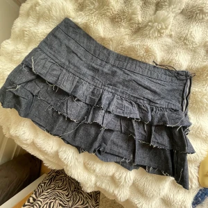 Mörkgrå volangkjol med dragkedja - Supersöt mörkblå kortkjol med flera lager volanger och råa kanter för en edgy vibe. Kjolen har dragkedja i sidan och är gjord i ett jeansliknande material. Perfekt för att styla med boots eller sneakers för en cool look. Använd nån gång bara.