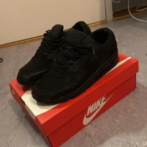 Nike Air Max 90 Black sneakers - Snygga Nike Air Max 90 i helsvart färg. Skorna har en chunky sula med synlig Air-enhet, mesh och skinnpaneler samt klassisk snörning. Perfekta för dig som gillar en clean och stilren look med streetkänsla.