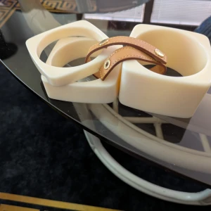 Louis Vuitton chunky armband i vitt äkta vintage 3 stycken - Unika chunky armband från Louis Vuitton i vit plast med fyrkantig form och detaljer i ljust brunt läder med guldiga nitar. Perfekt statement piece för dig som vill sticka ut med lyxig och cool accessoar.