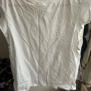 Vit blus med broderade detaljer - Säljer en söt vit blus med korta ärmar och broderade spetsdetaljer framtill. Blusen har ett diskret hålmönster och är tillverkad i mjuk bomull, perfekt för en fräsch och somrig look. Passar lika bra till jeans som till kjol.