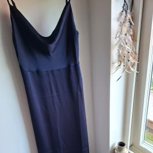 Mörkblå långklänning från Vila - Supersnygg mörkblå långklänning från Vila med tunna axelband och draperad urringning. Klänningen har en elegant, slät yta och rak passform som faller snyggt längs kroppen. Perfekt för dig som gillar stilrena och minimalistiska looks. Önskas fler bilder hur passformen är går det att efterfråga. Dock är klänningen för stor på mig därav anledning till varför den säljs. 