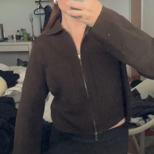 Brun stickad cardigan jacka från Å - Mysig brun stickad cardigan jacka från Å med dragkedja framtill och klassisk krage. Jackan har lång ärm och en croppad passform som ger en chill vibe. Perfekt att slänga på sig över en t-shirt eller linne för en snygg lager-på-lager-look. Nypris är 600