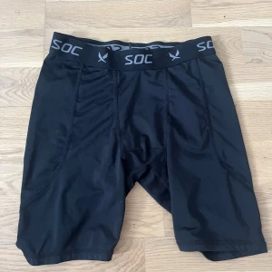 Svarta träningstights shorts från SOC - Svarta, tighta träningstights shorts från SOC med elastisk midja och logga runt hela linningen. Gjorda i ett syntetmaterial som andas och håller dig torr under träningen. Perfekta för sport eller gympass när du vill ha maximal rörelsefrihet.