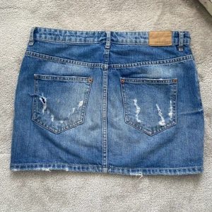 Blå jeanskjol från Perfect Jeans - Snygg blå jeanskjol från Perfect Jeans med slitna detaljer och rå kant nertill. Klassisk femficksmodell med bälteshällor och knappstängning. Perfekt för dig som gillar en avslappnad och trendig stil. Kjolen är lågmidjad och så snygg! 