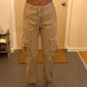 Beiga cargopants med snörning - Säljer ett par beiga cargopants med elastisk midja och snörning. Byxorna har stora fickor på sidorna och resår vid bensluten för en avslappnad vibe. Perfekta för en chill och streetig look.