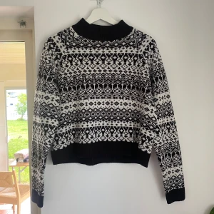 Svartvit stickad tröja från Monki - Säljer en svartvit stickad tröja från Monki. Tröjan har en lite högre, ribbad krage och långa ärmar. Den är väldigt varm att ha på sig, men är lite kort på magen. 