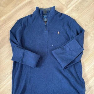 Marinblå half zip tröja Polo Ralph Lauren - Snygg marinblå långärmad tröja från Polo Ralph Lauren med half zip och klassisk broderad logga på bröstet. Tröjan är i mjuk bomull och har en ribbad krage samt grå insida vid halsen. Perfekt för en chill och stilren look.