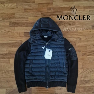 Svart Moncler Cardigan - Letar du efter den perfekta jackan inför våren? ☀️ Denna Moncler cardigan har quiltad dunfront och stickade ärmar för en stilren look. Observera att den är liten i storleken. Denna passar mer som M, trots att det står xl. Perfekt för både vardag och fest.   ✔ Lyxig design – Quiltad dun och stickat material. ✔ Praktisk – Huva, dragkedja och fickor. ✔ Ikonisk touch – Moncler-logga på ärmen.  Mått: Axelbredd: 46 cm, Längd: 62 cm, Pit to pit: 54 cm.  📌 Skick: Endast provad – nyskick! 📦Snabb leverans📦