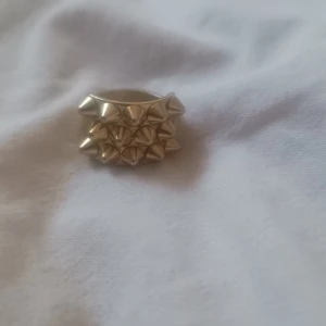 EDBLAD guld ring med nitar  - Säljer en guldfärgad ring dekorerad med spetsiga nitar. Perfekt, ringen har en bred design som gör den till ett statement-smycke. Storlek 18.50, knappt använd.
