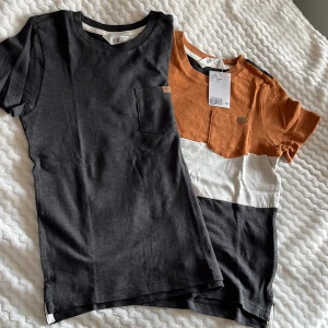 Två t-shirts från H&M i svart och orange - Säljer två snygga t-shirts från H&M. En är helsvart och den andra är i blockfärger med orange, vit och svart. Båda har en liten bröstficka och är kortärmade. 
