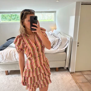 Mönstrad klänning med volanger - Säljer världens finaste mönstrade klänning från Sandro! Den är köpt i en fransk storlek 42 och är efter detta insydd smått vid midjan så skulle säga att den passar mer en 38. Såå så fin passform! 🩵