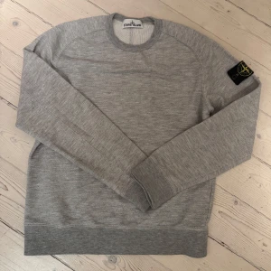 Grå tröja från Stone Island - Säljer en stilren grå tröja från Stone Island. Tröjan har långa ärmar och en rund halsringning. Den är tillverkad i ett mjukt material och har en ikonisk logga på ärmen. Perfekt för en avslappnad och trendig look.