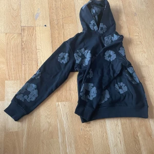 Svart hoodie från Denim Tears - Säljer en svart hoodie från Denim Tears med gråa blommönster. Den har en klassisk design med huva och långa ärmar. Perfekt för en avslappnad stil. 🌼!skriv privat för mer information!