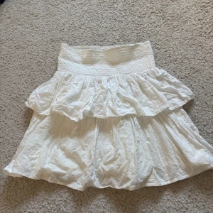 Vit kjol med volangdetaljer - Charmig vit kjol med volangdetaljer och elastisk midja. Kjolen har ett broderat mönster och de är storlek 170 så ungefär en S