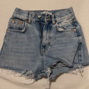 Ljusa jeansshorts från Pull&Bear - Snygga ljusa jeansshorts från Pull&Bear med fransiga kanter och slitna detaljer. Perfekta för en avslappnad sommarlook. De har en klassisk femficksdesign och knappgylf.