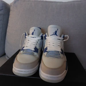 Nike Air Jordans 4 i vit och blå - Säljer ett par Nike Air Jordans 4 i en snygg kombination av vit och blå. Skorna har klassisk snörning och en ikonisk design med synlig luftdämpning i sulan. Perfekta för dig som vill ha både stil och komfort.