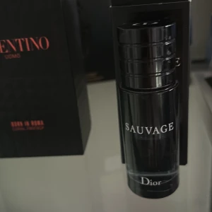 Dior Sauvage Parfym - Säljer en elegant och maskulin parfym från Dior, Sauvage. Flaskan är stilren och svart med en modern design. Perfekt för den som vill ha en tidlös doft med en fräsch och kryddig karaktär.
